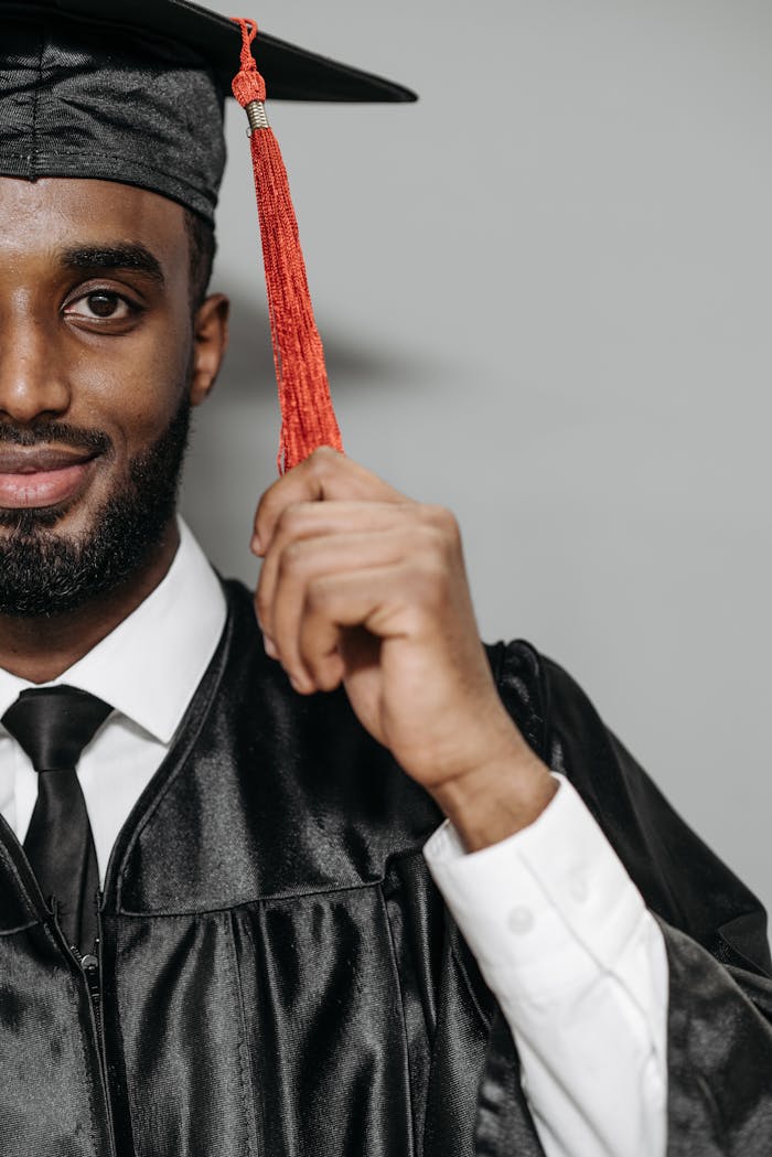 Half-face portrait of a smiling graduate holding a red tassel, wearing a cap and gown.